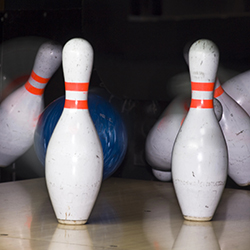 A bowling ball hitting a set of bowling pins, representing the idea of a bowl-a-thon.