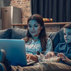 A mother and son attending a virtual movie night fundraiser on their couch.