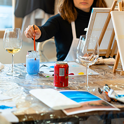 A paint and sip participant painting while enjoying a beverage beside them, illustrating how this fundraising idea works.
