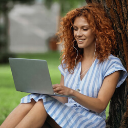 A virtual tour participant sitting with a laptop in a park.